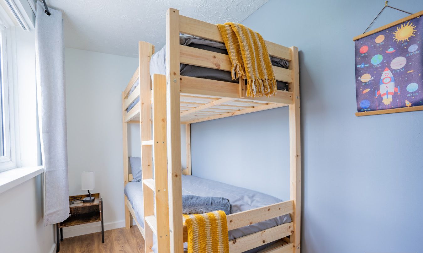A bunk bed room with a window, a small table, and a wall decoration.