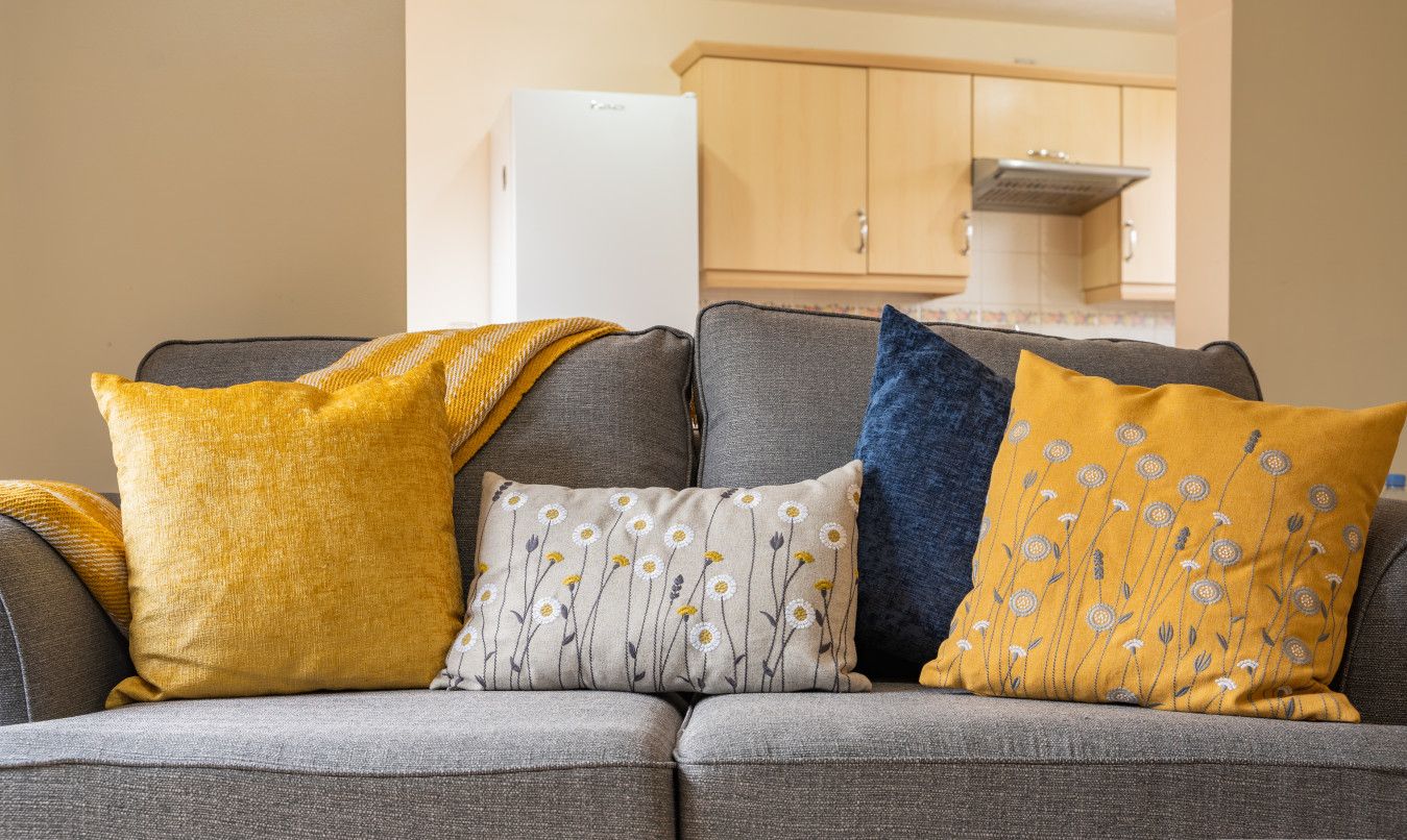 A grey sofa with four pillows in yellow, blue, white, and mustard colors.