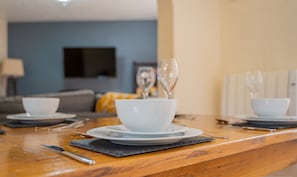 Une table à manger dressée avec des bols et des assiettes blancs, un couteau et des verres à vin.