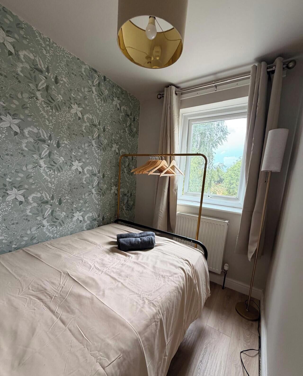 Een compacte, verzorgde kamer met een enkel bed, een raam met gordijnen, een radiator en een lamp.