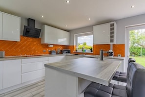 A modern kitchen with white cabinetry, a large island, and a view of greenery outside. - Jodi's Bungalow, Parking & Large Garden (Ruddington)