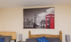 A hotel room with two beds, a large cityscape painting on the wall, and a red telephone booth. - Rocester Rest - Near to JCB+Alton Towers, Netflix (Alton Towers & Staffordshire Villages)