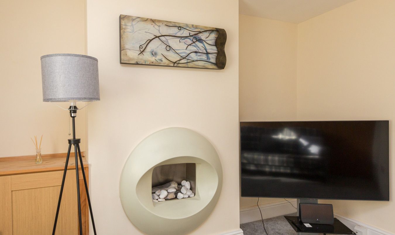A modern room with a flat-screen TV, a lamp, a fireplace, and a piece of abstract art on the wall.