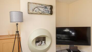 A modern room with a flat-screen TV, a lamp, a fireplace, and a piece of abstract art on the wall.