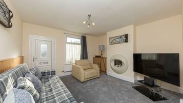 A living room with a sofa, armchair, fireplace, TV, and a lamp.