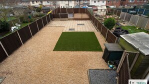 Un jardin avec un espace recouvert de gravier, une pelouse verdoyante et une clôture en bois.
