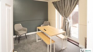 Une pièce avec un mur gris, une table en bois, deux chaises, un banc et une fenêtre avec des rideaux gris.