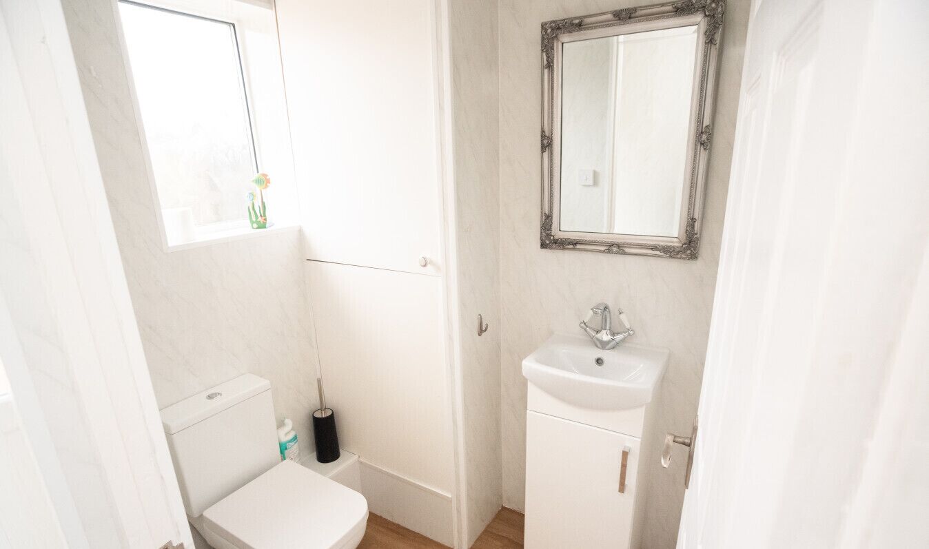 Et lille badeværelse med hvid indretning, toilet, vask og spejl.