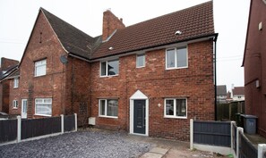 A two-story brick house with a front door, multiple windows, and a gravel driveway. - Sherwood Pines  Big Garden (Nottingham)
