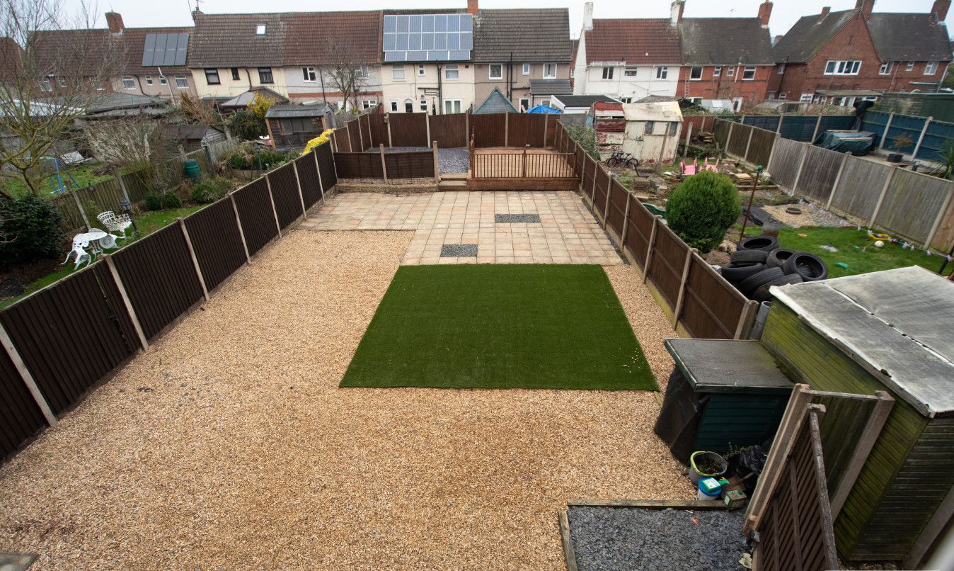 A backyard with a gravel area, a green lawn, and a wooden fence.