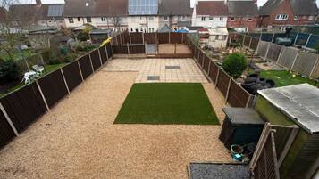 A backyard with a gravel area, a green lawn, and a wooden fence.