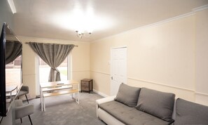 A room with a grey sofa, a small table, a chair, a TV, and a window with curtains. - Sherwood Pines  Big Garden (Nottingham)