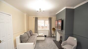 A living room with a sofa set, a television, a fireplace, and a chair.