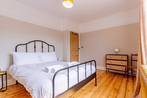 A bedroom with a metal-framed bed, wooden floor, a wooden dresser, and a door in the background. - Felicity's House with Hot Tub! (Queniborough)