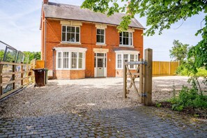 A two-story brick house with a gravel driveway and a wooden gate. - Felicity's House with Hot Tub! (Queniborough)
