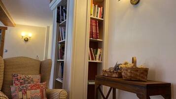 Una sala de estar acogedora con un sillón estampado, una estantería llena de libros y una mesita de madera con objetos decorativos.