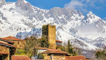 A historic stone tower amidst snow-covered mountains, with traditional red-tiled buildings in the foreground.