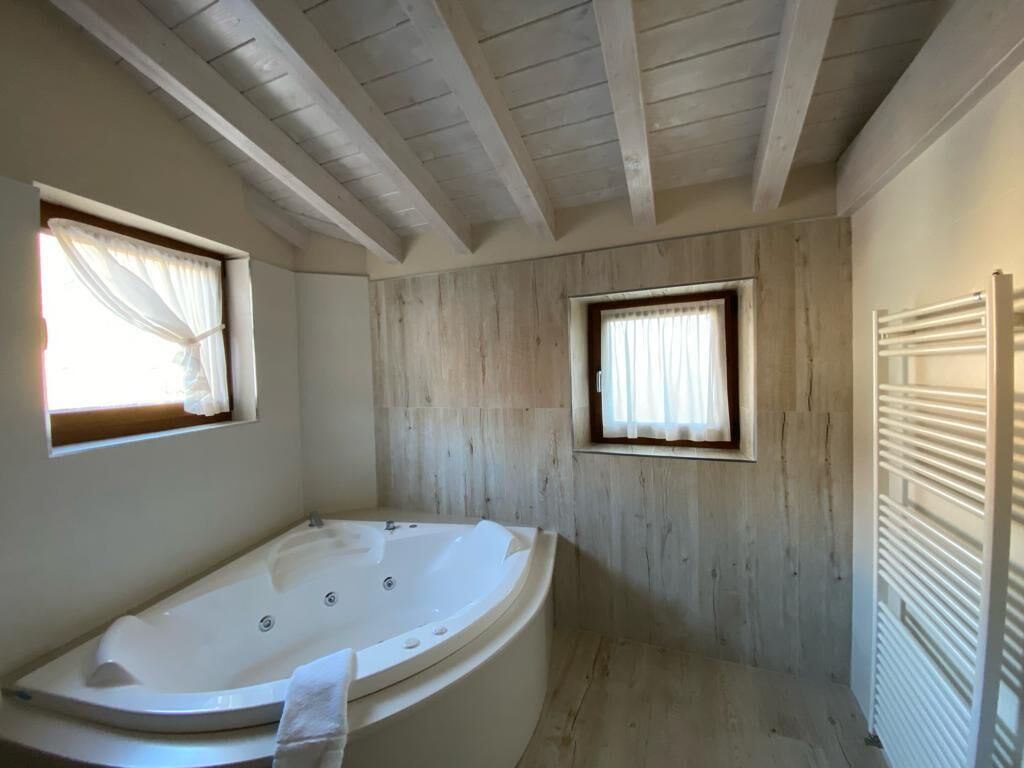 A bathroom with a freestanding bathtub, wooden walls, and a window with curtains.