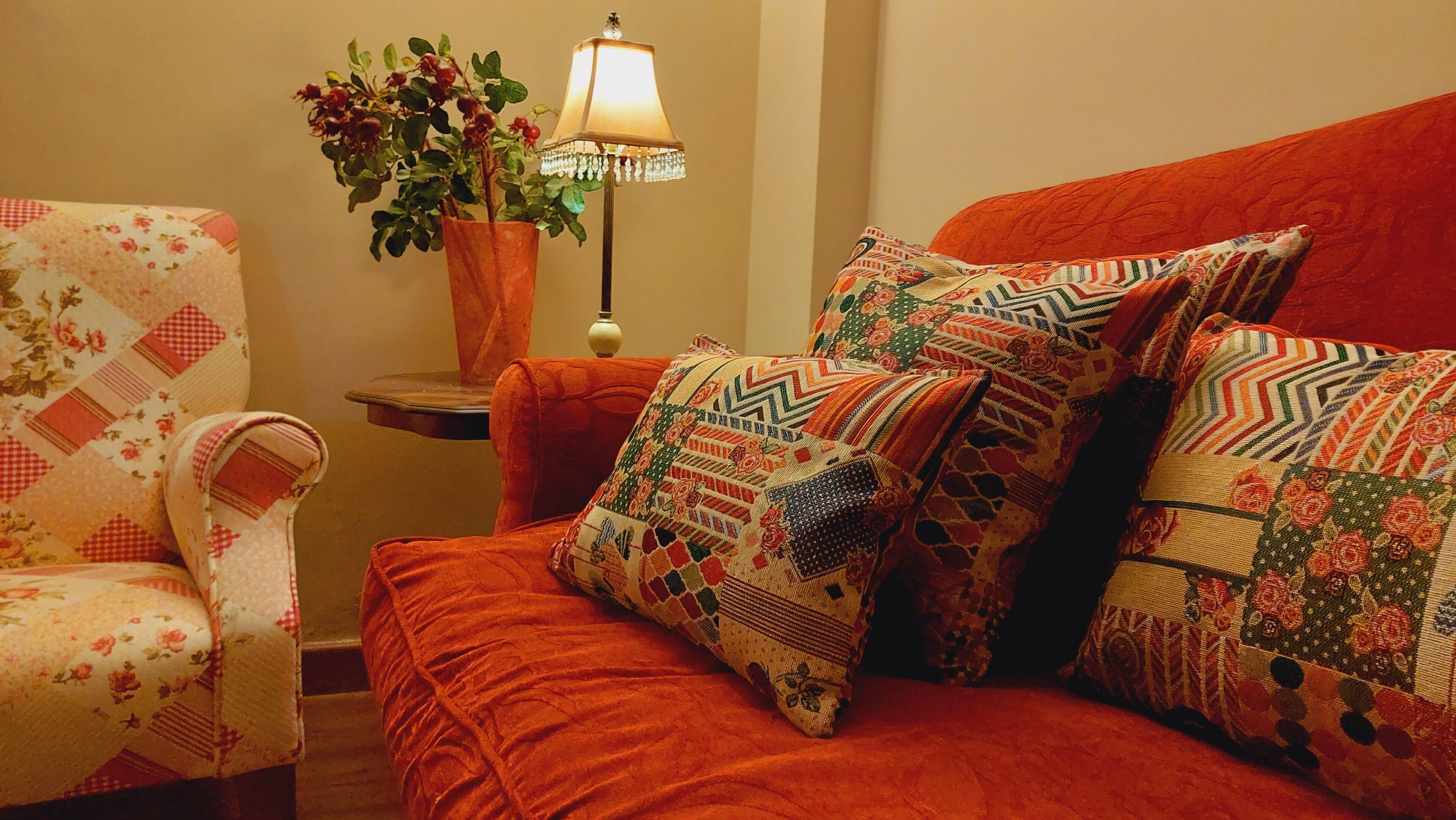 A cozy room with a red sofa, a floral armchair, and a table with a lamp and a plant.