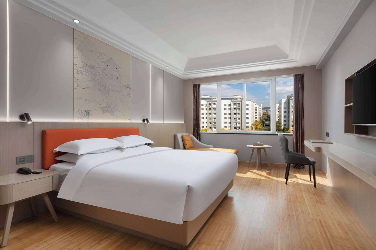 A modern hotel room with a large bed, a desk, a chair, a small table, and a TV.