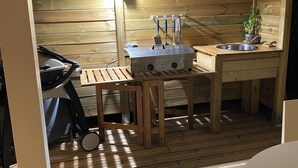 A compact wooden cabin with a kitchenette, a small table, and a grill.