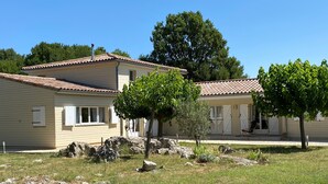 A two-story building with a tiled roof, a small garden area with rocks and a few trees, and a clear blue sky in the background.