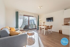 A modern living room with a sofa, chairs, a dining table, and a kitchen area. - Lakefront T2 Apartment – Rive du Lac (Menthon-Saint-Bernard)