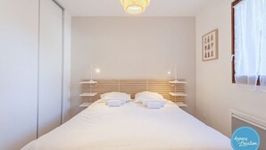 A bedroom with a bed, bedside lamps, a headboard, and a window with curtains.