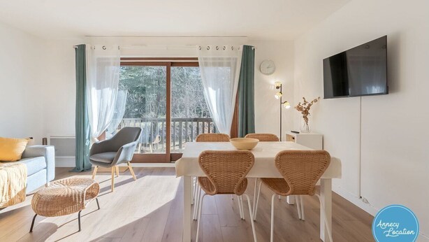 A modern living room with a dining area, a sofa, a chair, a TV, and a balcony with curtains.
