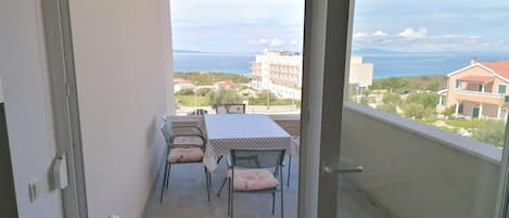 A balcony with a table and chairs, a view of the sea and buildings in the distance.