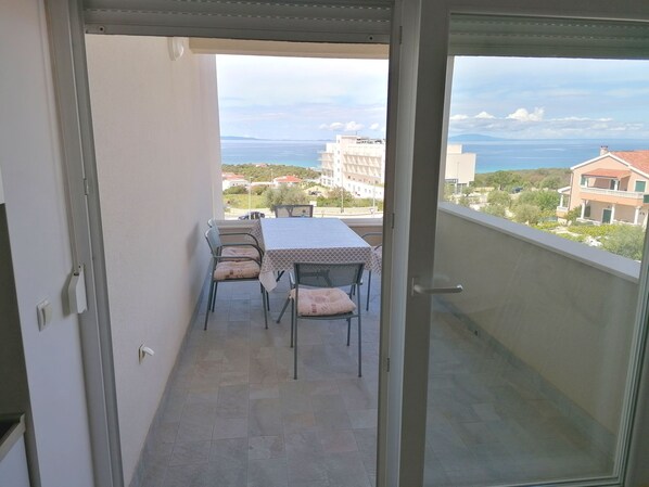 A balcony with a table and chairs, a view of the sea and buildings in the distance.
