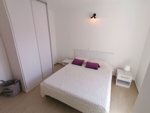 A bedroom with a bed, a nightstand, a lamp, a wardrobe, and a trash bin.