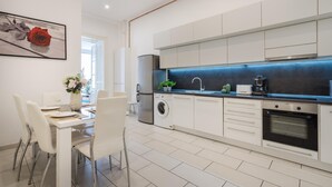 A modern kitchen with white cabinetry, a built-in oven, a washing machine, and a dining area with a table and chairs. - Spacious Stay at Bank Center   Parlament Neighbor (Budapest)
