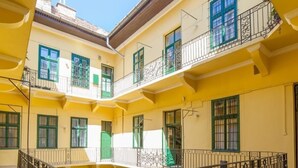 A yellow multi-story building with balconies, a central courtyard, and potted plants. - Spacious Stay at Bank Center   Parlament Neighbor (Budapest)