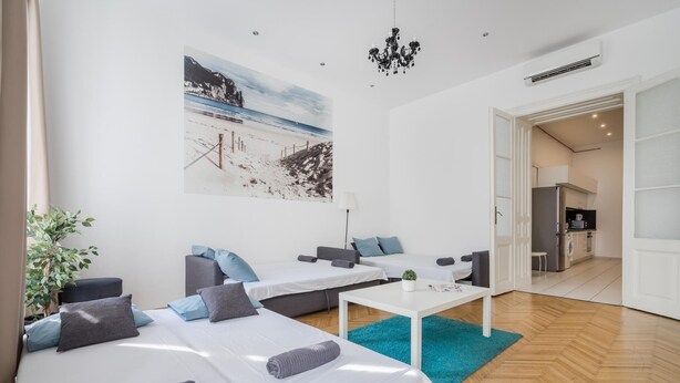 A modern hotel room with two beds, a dining table, a small kitchen, and a large beach mural on the wall. - Spacious Stay at Bank Center   Parlament Neighbor (Budapest)