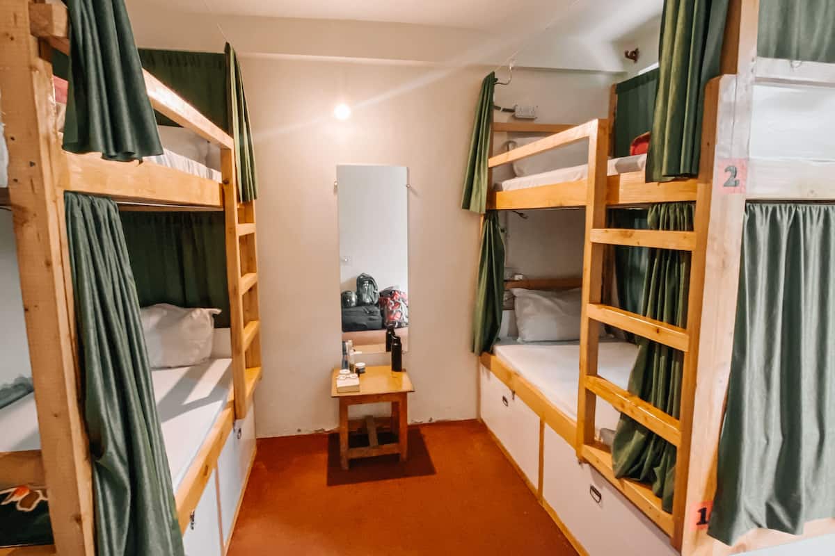 A dormitory room with bunk beds, a small table with toiletries, and a mirror.