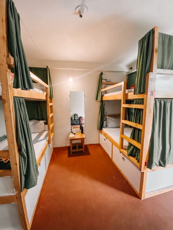 A dormitory room with bunk beds, a small table with toiletries, and a mirror.