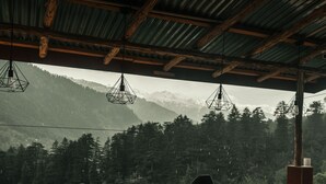 A person sitting at a wooden table with a view of a forested mountain range. - Jungle by sturmfrei Manali (Manali)