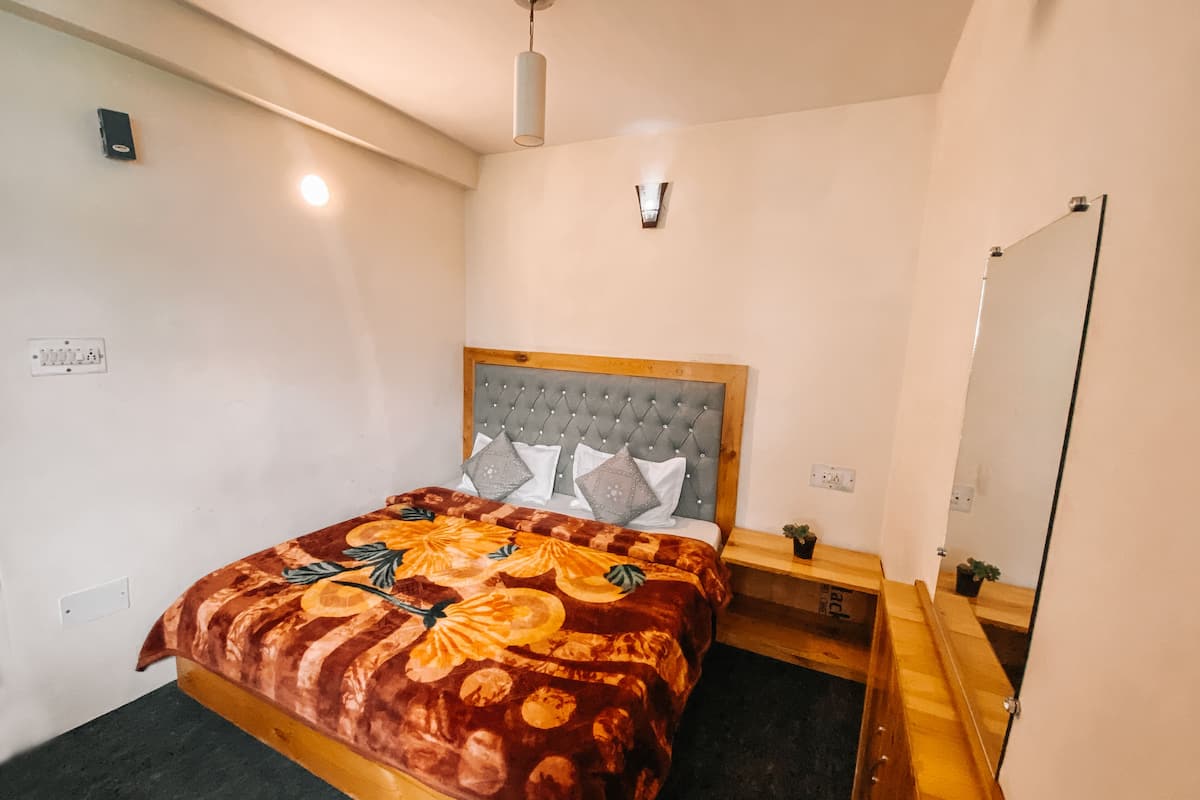 A bedroom with a bed, a wooden headboard, a bedside table, a mirror, and a ceiling light fixture.