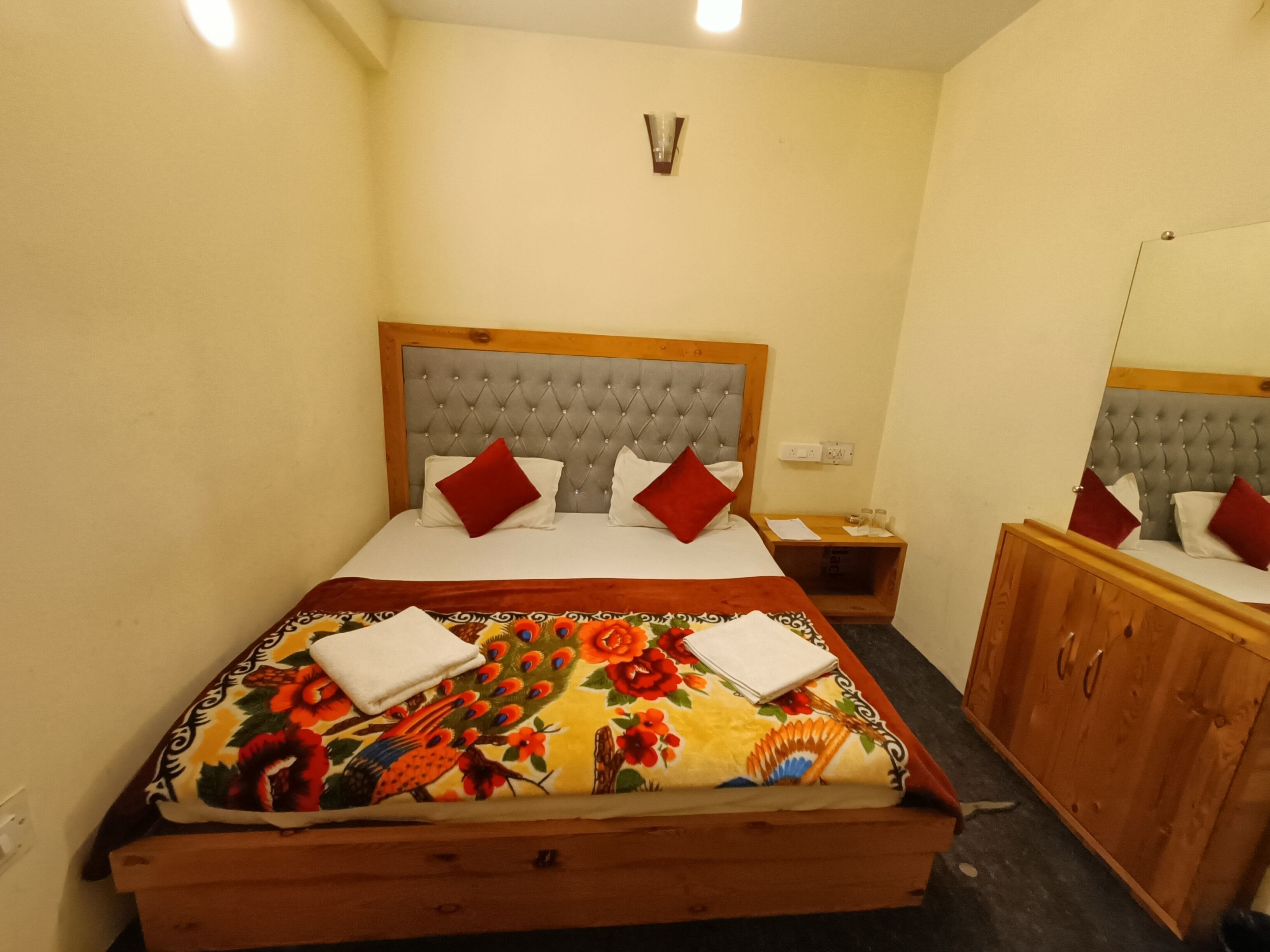 A hotel room with a bed, a wooden nightstand, a mirror, and a wardrobe.