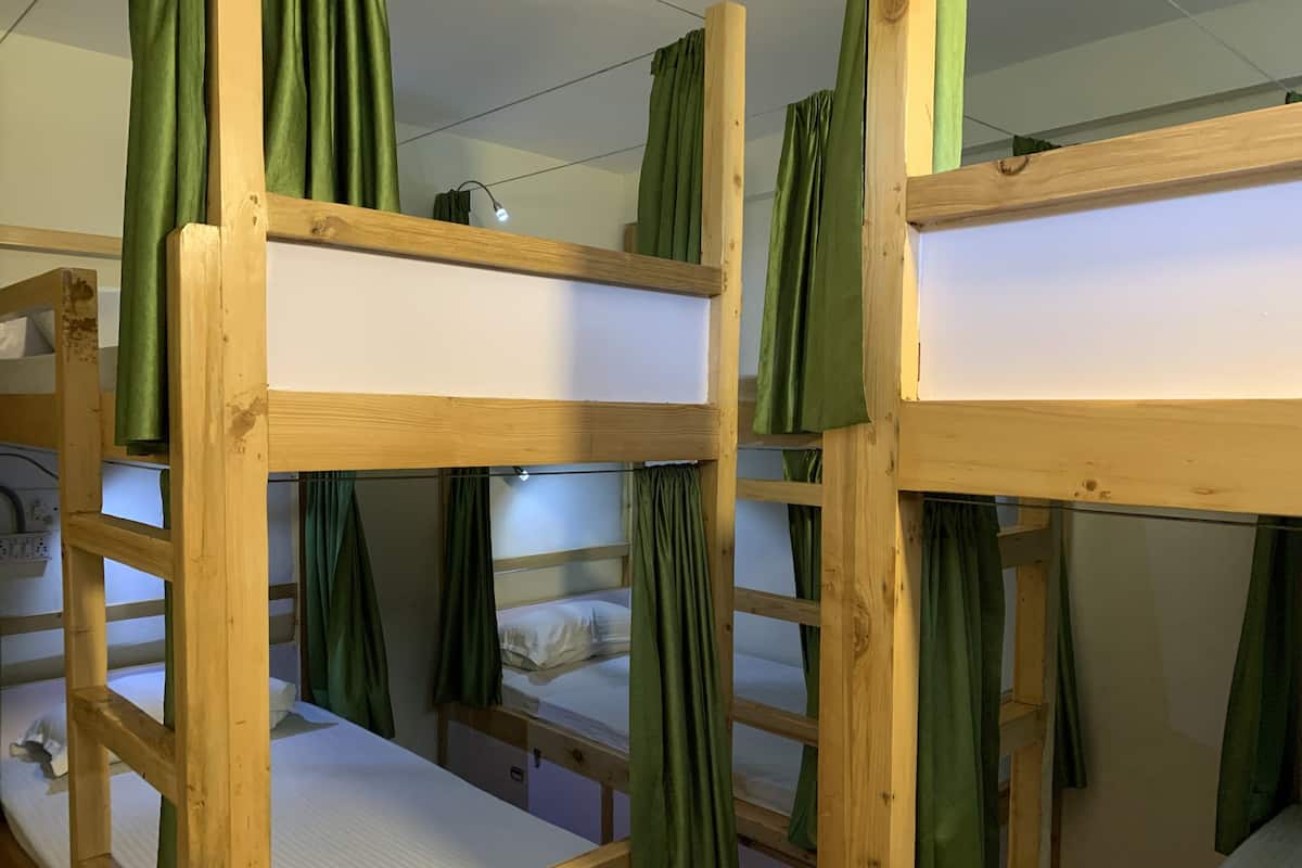A bunk bed room with green curtains, wooden frames, and a white mattress.