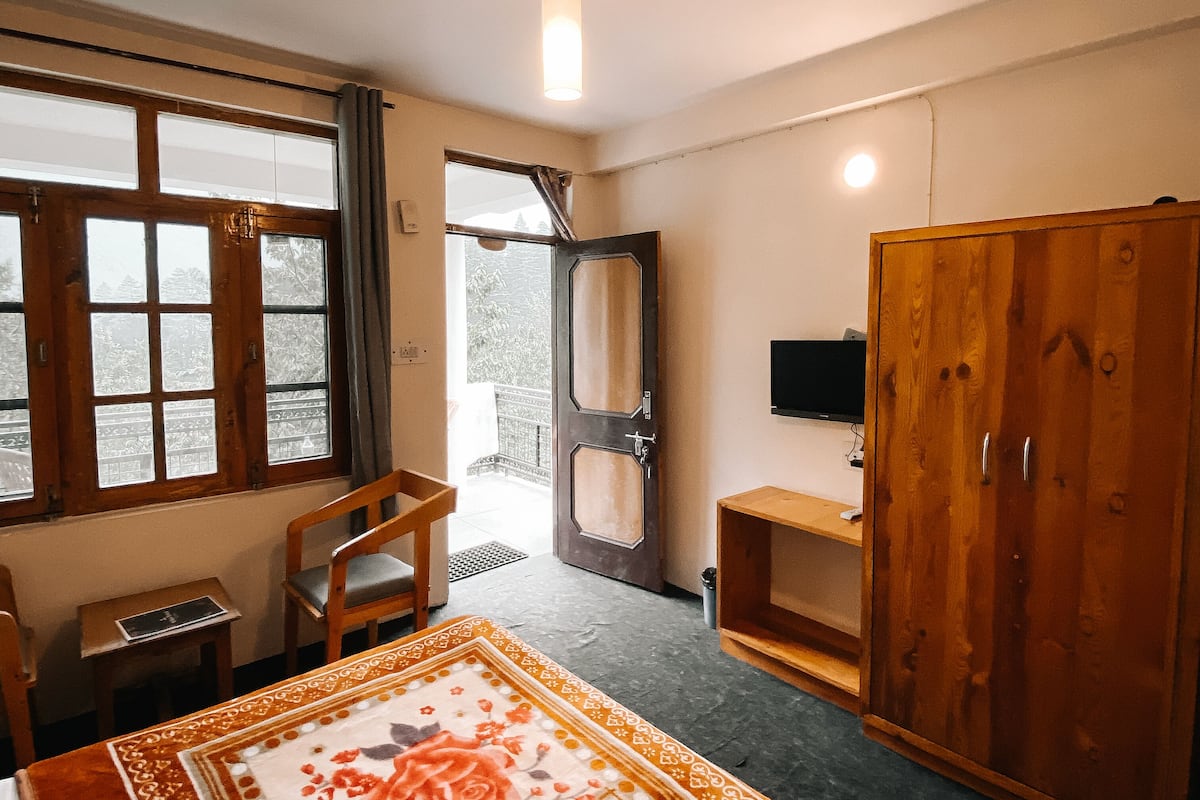 A room with a bed, a desk, a wardrobe, a television, and a window with curtains.