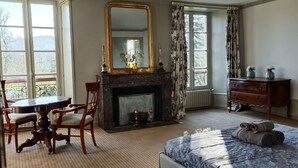 Une chambre à coucher avec un lit, une cheminée, une table avec des chaises et une commode.