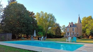 Une piscine rectangulaire bordée d’une terrasse en pierre, entourée d’une pelouse verdoyante et d’arbres.