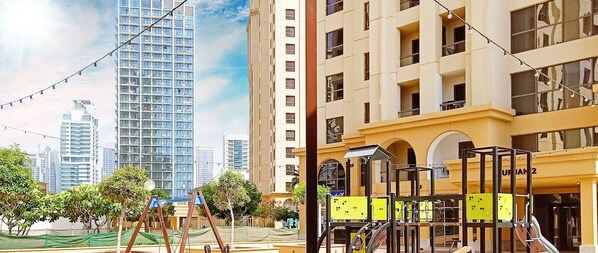 A modern building with a yellow facade, large windows, and a playground area with swings and a slide. - LUX The JBR BlueWaters View Suite 2 (Dubai)