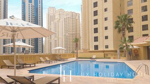 A poolside area with lounge chairs and umbrellas, surrounded by high-rise buildings. - LUX The JBR BlueWaters View Suite 2 (Dubai)