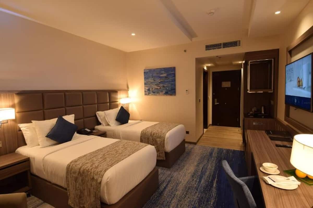 Een hotelkamer met twee bedden, een bureau, een televisie en een schilderij aan de muur.
