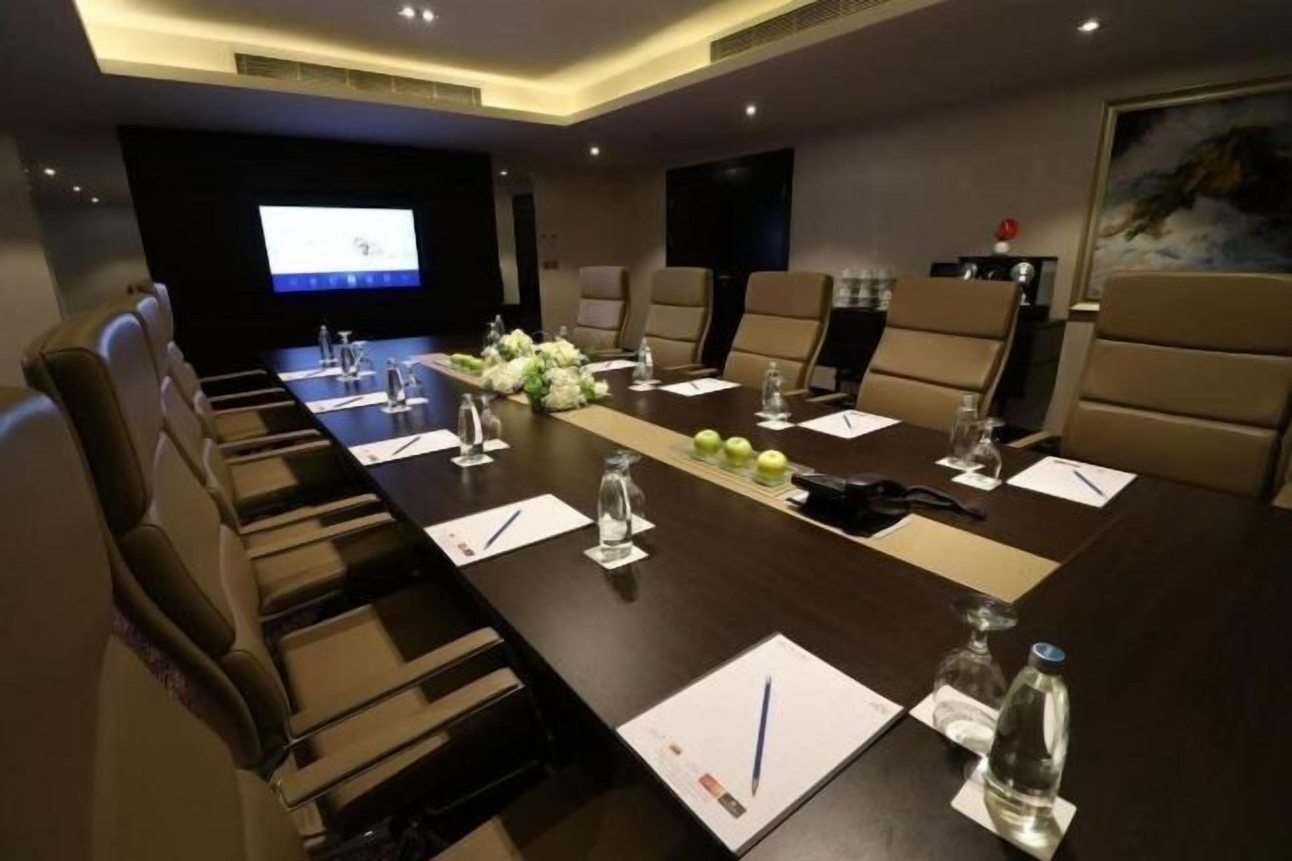 A conference room with a long table, chairs, a projector screen, and a painting on the wall.