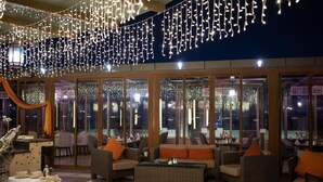 Un espace extérieur aménagé avec des meubles en osier et des coussins orange, décoré de guirlandes lumineuses.