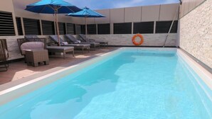 Une piscine avec des chaises longues et des parasols, une bouée de sauvetage et un mur en pierre.